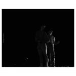 The silhouette of two performers close together on stage
